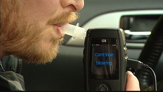Un homme souffle dans un appareil à l'intérieur d'une voiture pour tester son taux d'alcoolémie.