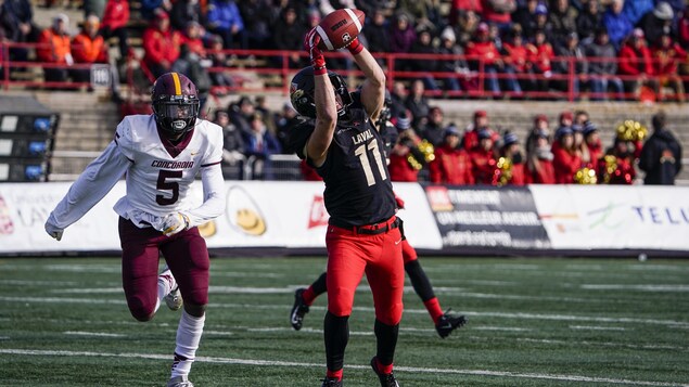 Un joueur de football du Rouge et Or s'étire pour capter un ballon devant un joueur des Stingers.