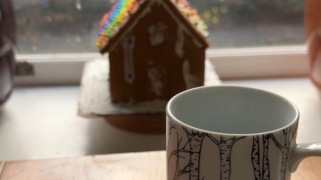 Une tasse sur une table et une maison en pain d'épices derrière.
