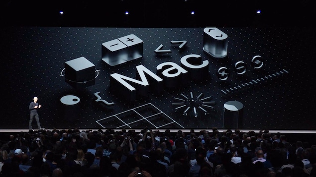 Une capture d'écran de la présentation d'Apple montrant Tim Cook sur la scène d'un amphithéâtre avec le mot « Mac » affiché à l'écran derrière lui. Une capture d'écran de la présentation d'Apple montrant Tim Cook sur la scène d'un amphithéâtre avec le mot « Mac » affiché à l'écran derrière lui.