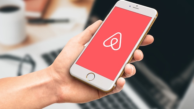 Une main tient un téléphone portable muni de l’application Airbnb.