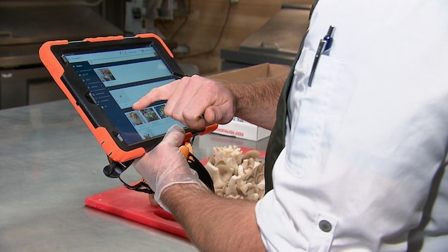 Un cuisinier tient une tablette électronique affichant l'application Octogone. 