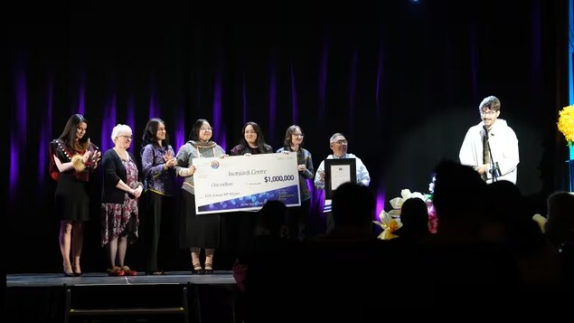 A group of people hold up a giant check on stage. 