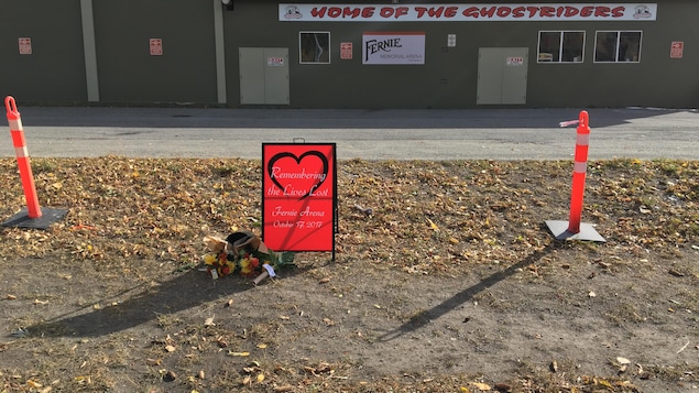 Des fleurs et une affiche avec un coeur déposés devant un aréna Des fleurs et une affiche avec un coeur déposés devant un aréna