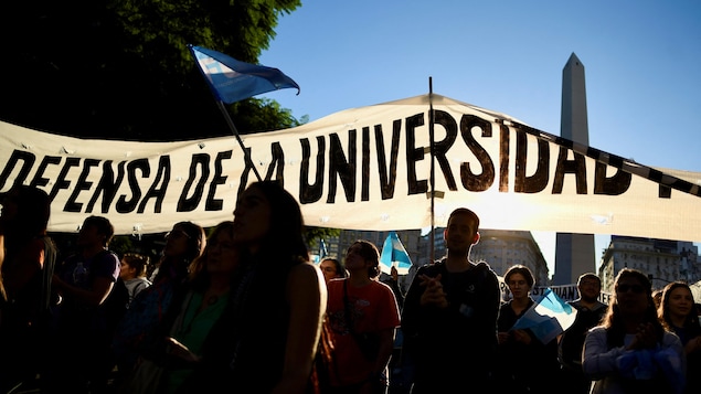 En contrejour, des manifestants tiennent une banderole et des drapeaux argentins.