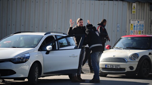 Un homme lève les mains dans les airs pendant qu'un policier procède à une fouille en règle.