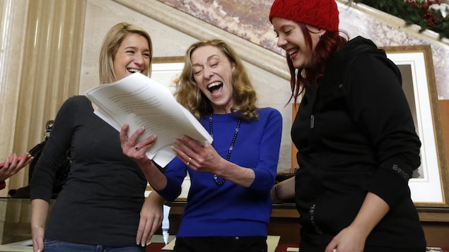 Trois femmes réagissent avec des grands sourires en consultant un document écrit.