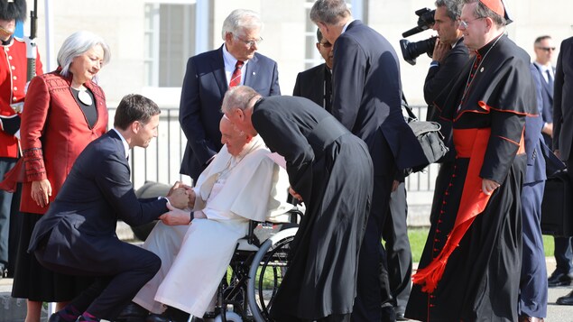 Justin Trudeau s'accroupit devant la chaise roulante du pape François pour lui serrer la main.