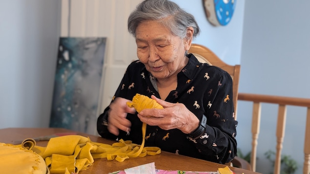 Une dame âgée tourne des lanières de suède pour en faire une pelote.