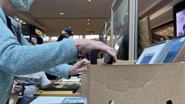 Une personne âgée fouille une boîte qui contient des œuvres d'art, au centre commercial Saint-Vital, le 2 octobre 2022. 