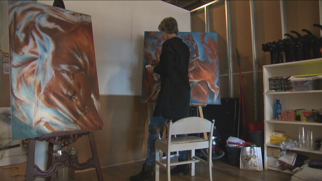 Une femme peint de dos dans une galerie.