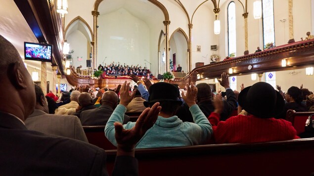 On voit, de dos, des fidèles assis, réunis en prière dans l'église baptiste d'expression française de Brooklyn. On voit, de dos, des fidèles assis, réunis en prière dans l'église baptiste d'expression française de Brooklyn.