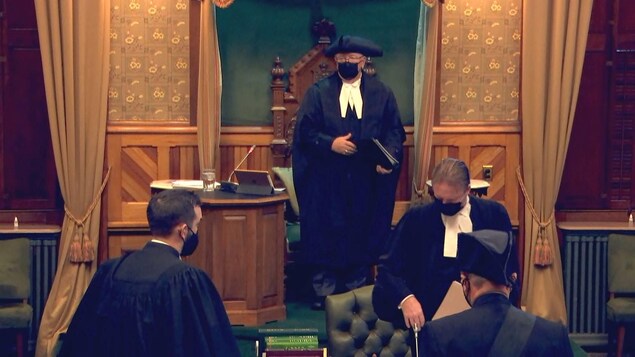 Le président de la Chambre et d'autres personnes vêtues de toges noires et le visage couvert d'un masque noir.