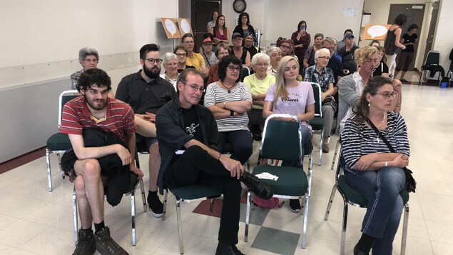 Des dizaines de personnes assises sur des chaises dans une salle. Des dizaines de personnes assises sur des chaises dans une salle.
