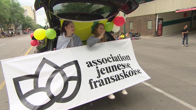 Deux jeunes femmes assises à l’arrière d’un véhicule montrent le logo de l’AJF durant le défilé.
