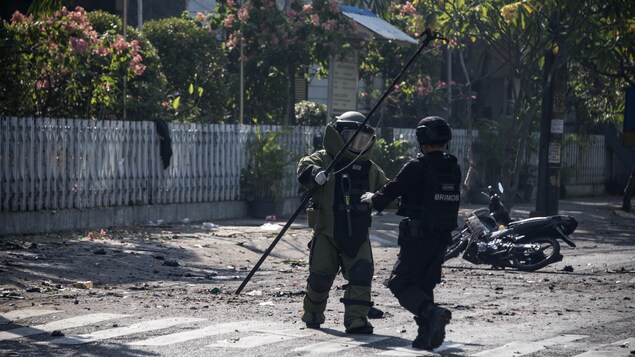 Un membre de l’escouade anti-bombe de la police indonésienne examine le site d’une explosion survenue à l’extérieur d’une église de Surabaya le 13 mai 2018