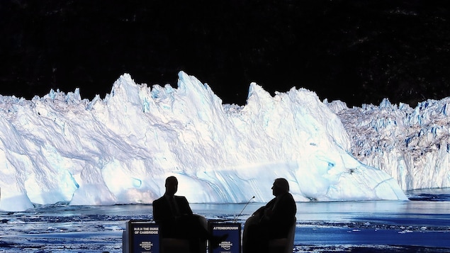Deux hommes assis côte à côte dans l'obscurité d'une salle dans laquelle sont projetées sur un écran des images de glaciers et d'eau.