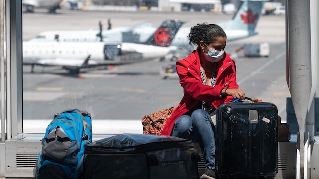 Une voyageuse assise avec ses valises à l'aéroport et des avions d'Air Canada sur le tarmac.