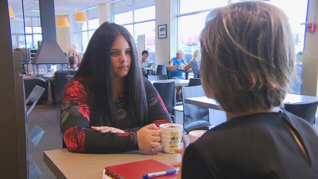 Jeune femme portant un chandail noir et rouge attablée dans un café. Jeune femme portant un chandail noir et rouge attablée dans un café.