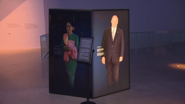 Un panneau dans une exposition portant l'image d'une femme asiatique sur son côté gauche est assombri tandis que le portrait d'un homme sur le côté droit est illuminé.