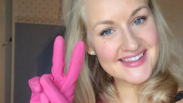 Une femme souriante avec des gants rose fait le signe de paix avec les doigts. 