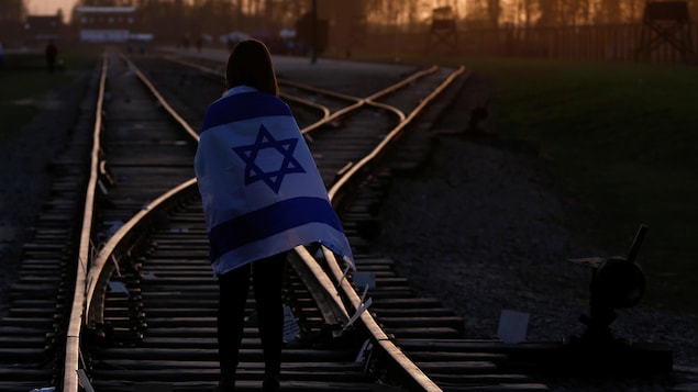 Au coucher de soleil, une femme marche sur des rails de chemin de fer et porte sur ses épaules un drapeau israélien. Au coucher de soleil, une femme marche sur des rails de chemin de fer et porte sur ses épaules un drapeau israélien.