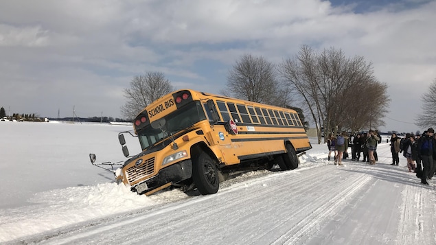 On voit à gauche un autobus dans un fossé avec plein d'enfants à droite qui rient et prennent des photos de l'autobus. On voit à gauche un autobus dans un fossé avec plein d'enfants à droite qui rient et prennent des photos de l'autobus.
