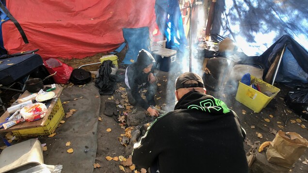 Deux occupants d'un camp de fortune se préparent un repas.