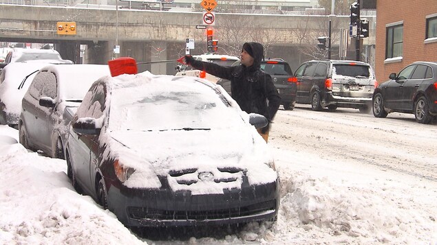 Un homme enlève la neige sur le toit d'une voiture avec une petite pelle.