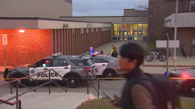 Des voitures de patrouille sont stationnées devant une école.