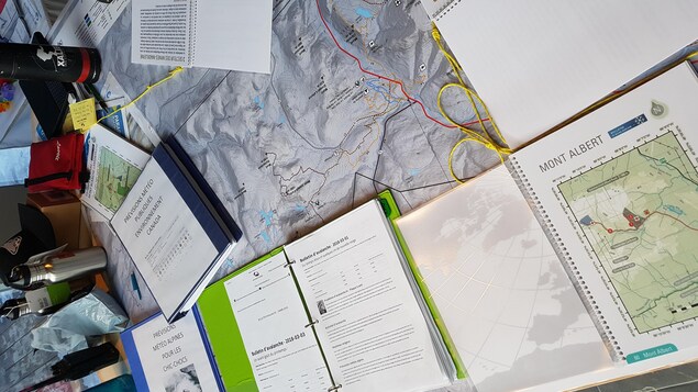 Plusieurs livres de prévisions météorologiques sont ouverts sur une table. Ils permettent de déterminer les risques d'avalanche dans le Parc national de la Gaspésie. 