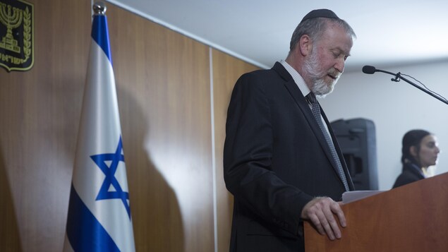 Avichaï Mandelblit parle derrière un lutrin et un drapeau d'Israël.