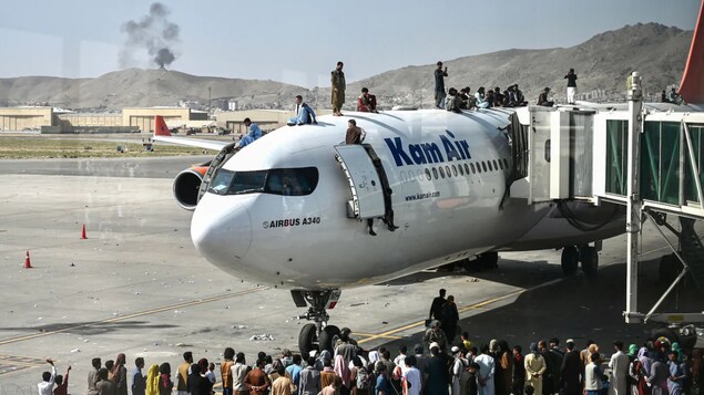 Des dizaines de personnes attendent devant et sur le dessus d'un avion à l'aéroport de Kabul.