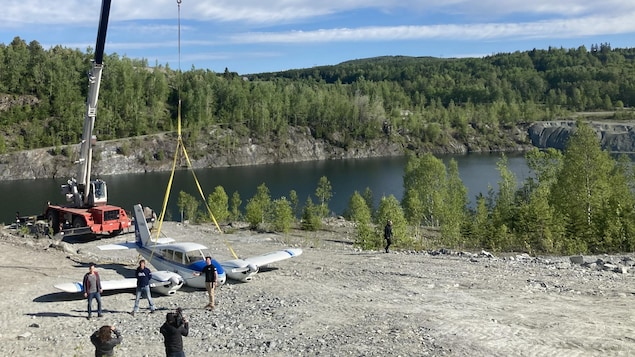 Un avion harnaché par les sangles d'une grue, aux abords d'une étendue d'eau