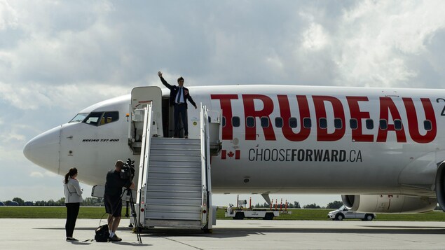Justin Trudeau salue de la main du haut de la rampe d'accès menant à l'avion du Parti libéral du Canada.