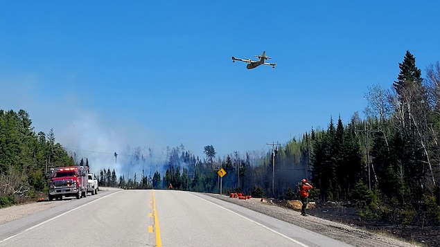 Un avion en approche d'un feu de forêt près d'une route.