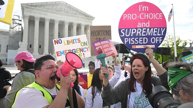 Des manifestantes pro-vie devant la Cour suprême des États-Unis, qui tiennent des pancartes. L'une d'entre elles crie dans un haut-parleur. 
