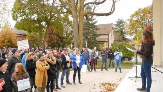 Des dizaines de manifestants regardent une femme prendre la parole au cours d'un rassemblement.