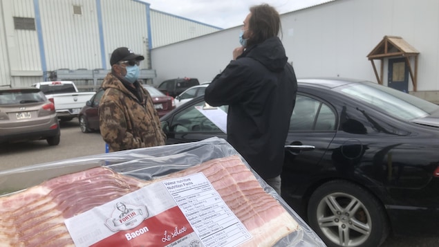 Deux hommes parlent dans un stationnement derrière un paquet de bacon en gros plan.
