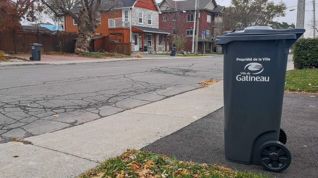 Un bac gris placé près du trottoir, près pour la collecte des ordures