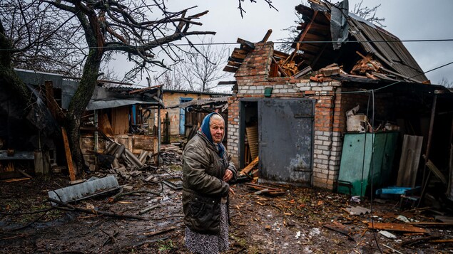Une femme âgée pose devant sa maison détruite par un obus.