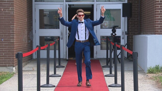 Un jeune homme en tenue de bal défile sur un tapis rouge à l'extérieur de l'école secondaire.
