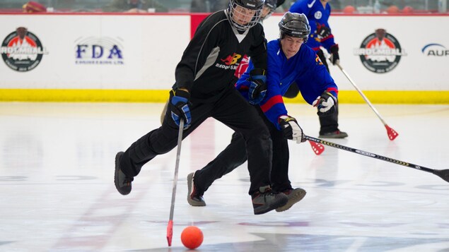 Deux joueurs de ballon sur glace avec leur équipement dans un aréna.