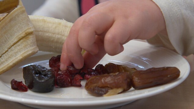 Petite main d'enfant dans une assiette remplie de bananes et  fruits secs.