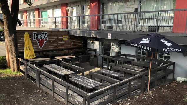 La terrasse d'un bar. La peinture des bancs et des clôtures en bois est défraîchie.
