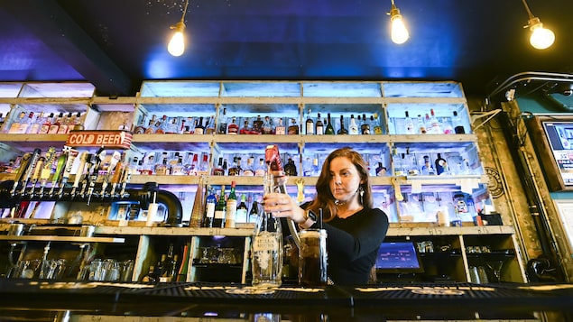 Une femme devant des étagères pleines de bouteilles d'alcool.