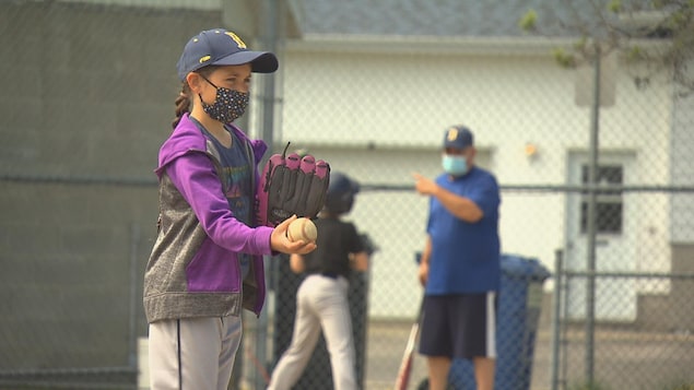 Une jeune qui tient une balle de baseball et qui s'apprête à lancer sur le terrain.