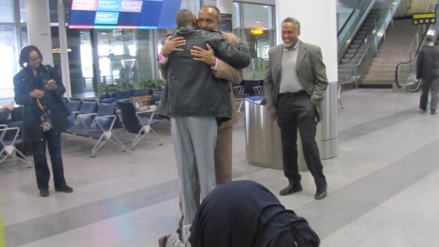 Bashir Makhtal à son arrivée à l'aéroport Pearson de Toronto dans les bras d'un homme. Une femme agenouillée embrasse le sol devant les deux hommes. Bashir Makhtal à son arrivée à l'aéroport Pearson de Toronto dans les bras d'un homme. Une femme agenouillée embrasse le sol devant les deux hommes.
