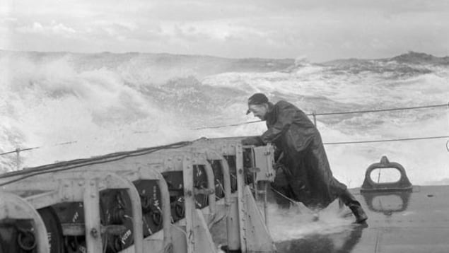 Un matelot non identifié vérifie l'arrimage des grenades sous-marines à la poupe de la frégate NCSM Matane, en grosse mer, au large des Bermudes en 1944.