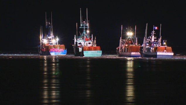 Quatre bateaux de pêche sur l'eau, la nuit.